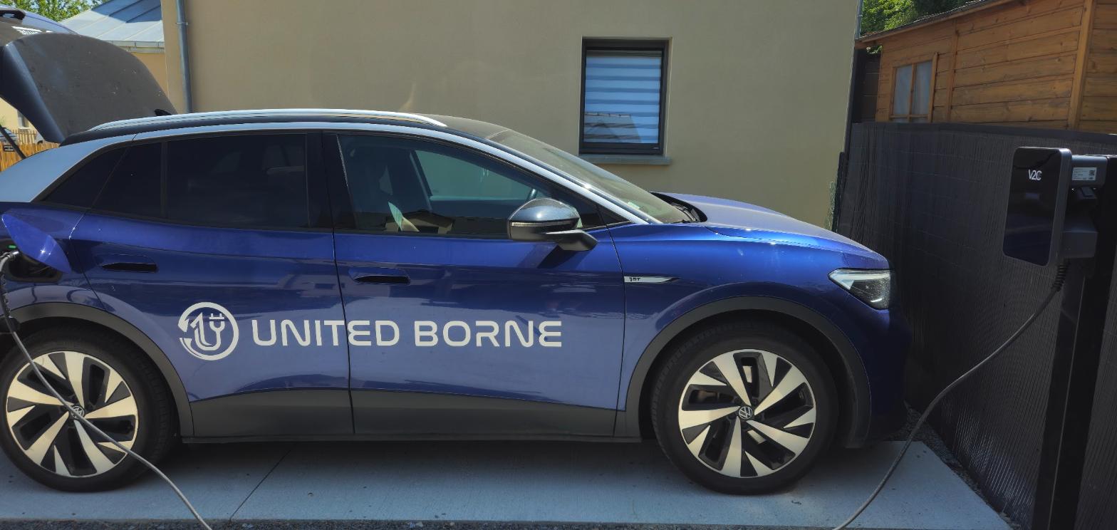 Voiture électrique aux couleurs de United Borne branchée sur une borne de recharge murale près de Cholet